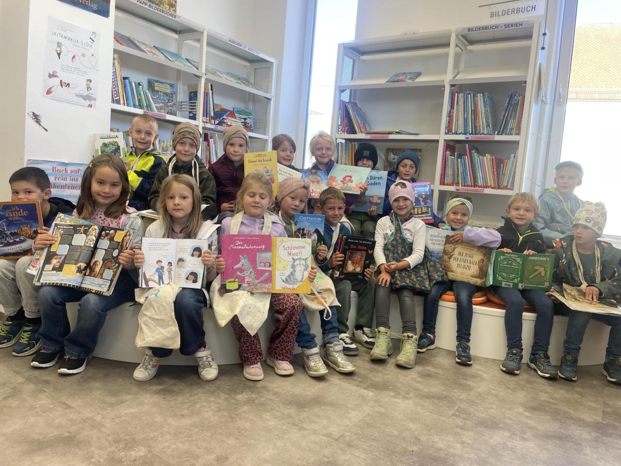Schülerinnen und Schüler der 1. Klasse Volksschule Herzogsdorf sitzen auf am Podest in der Bücherei.